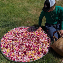 Load image into Gallery viewer, Person arranging rose petals on a large metal tray outdoors.
