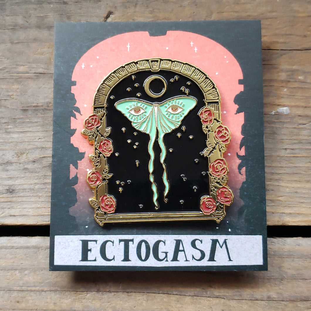 Luna Moth Enamel Pin. Design is of a luna moth in a starry archway, with eyes on its wings, and a crescent moon above it. The archway is surrounded by roses.